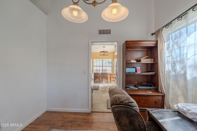 office space with baseboards, visible vents, wood finished floors, and a towering ceiling
