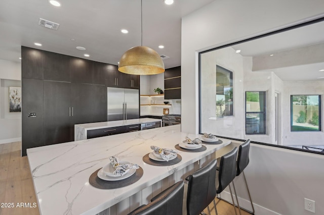 kitchen with hanging light fixtures, built in fridge, a breakfast bar area, and light stone countertops