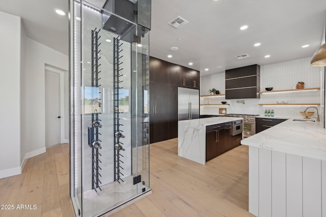 kitchen featuring sink, light stone counters, custom range hood, light wood-type flooring, and dark brown cabinets