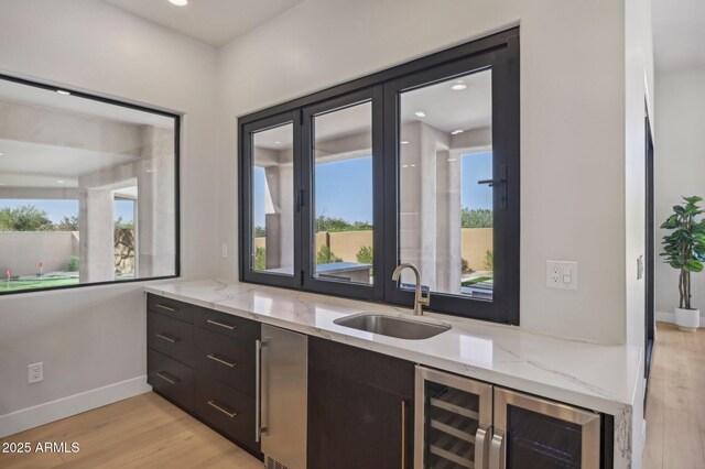 kitchen featuring sink, beverage cooler, light wood-type flooring, and light stone counters