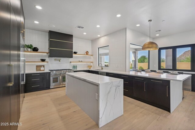 kitchen with sink, decorative light fixtures, wall chimney exhaust hood, a kitchen island, and high quality appliances