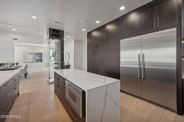 kitchen with built in appliances, light hardwood / wood-style flooring, light stone counters, and a center island