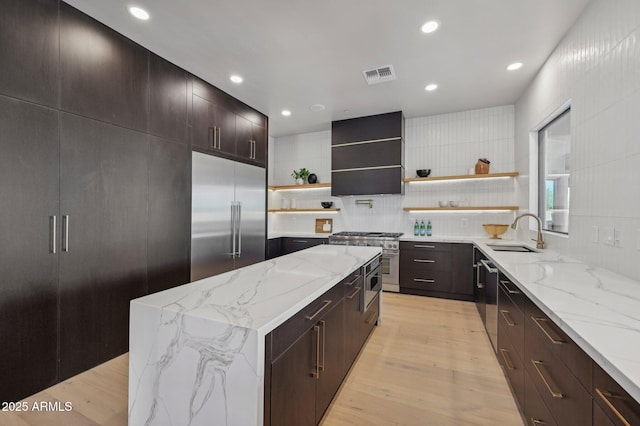 kitchen featuring sink, light stone counters, wall chimney range hood, a kitchen island, and high quality appliances