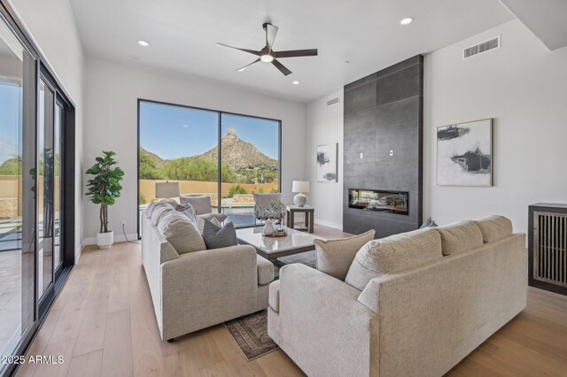 living room featuring light wood-type flooring, a tiled fireplace, ceiling fan, and a mountain view