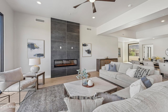 living room featuring a tiled fireplace, ceiling fan, and light hardwood / wood-style flooring