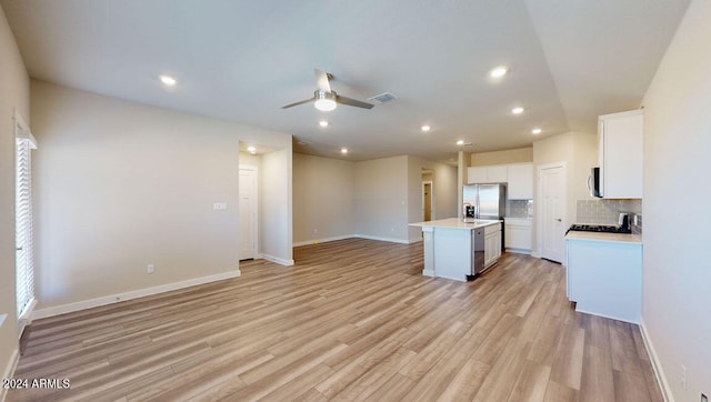 kitchen with white cabinetry, tasteful backsplash, stainless steel fridge, and an island with sink