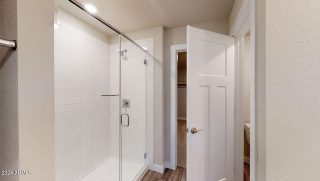 bathroom featuring wood-type flooring, a shower with door, and toilet