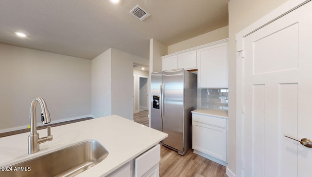 kitchen featuring sink, stainless steel refrigerator with ice dispenser, tasteful backsplash, white cabinets, and light wood-type flooring