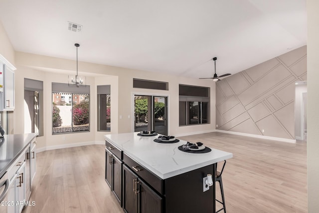 kitchen featuring light wood-type flooring, a kitchen island, pendant lighting, ceiling fan with notable chandelier, and white cabinets