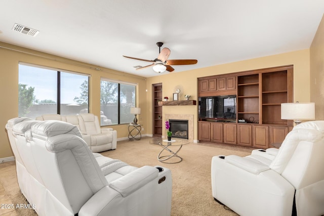 18171 W Marshall Ln, Surprise, AZ 85388 - living room featuring visible vents, light colored carpet, built in shelves, a tile fireplace, and a ceiling fan