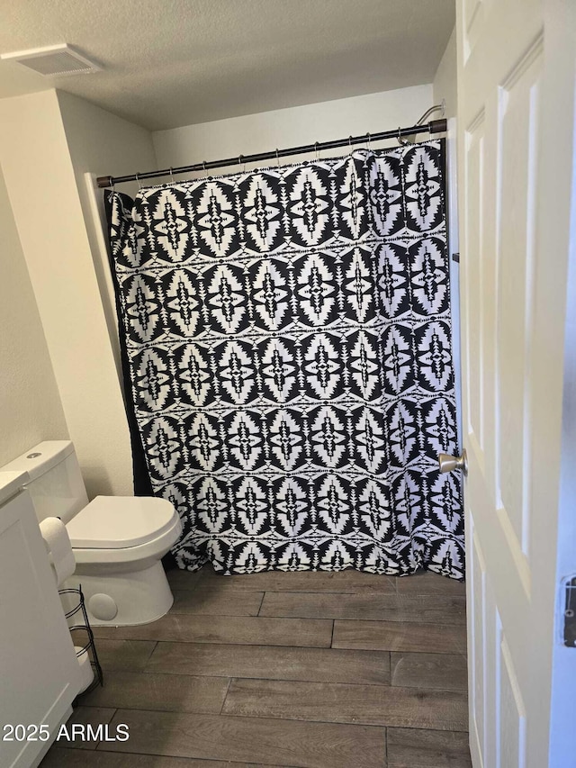 bathroom featuring toilet, wood-type flooring, walk in shower, and a textured ceiling