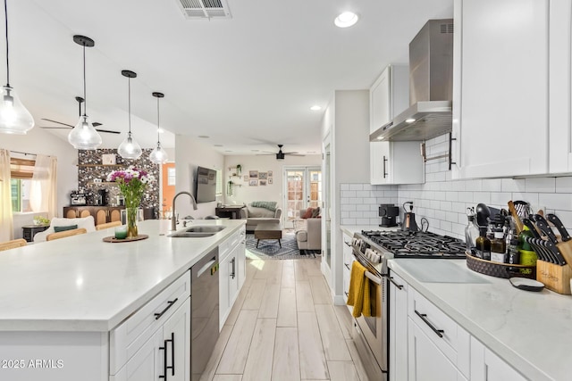 kitchen with visible vents, open floor plan, stainless steel appliances, wall chimney range hood, and a sink