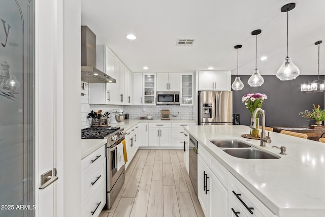 kitchen with stainless steel appliances, a sink, visible vents, wall chimney range hood, and backsplash