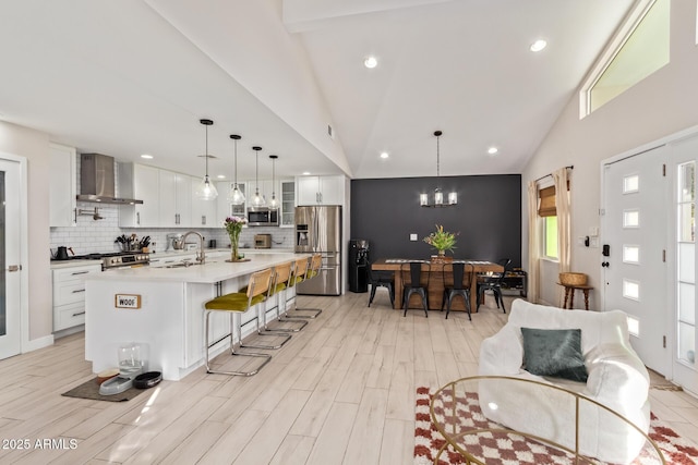 kitchen featuring a breakfast bar area, stainless steel appliances, light countertops, wall chimney range hood, and backsplash