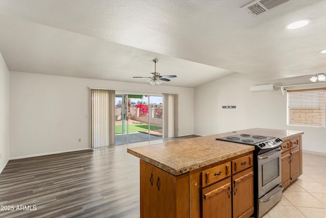 kitchen with visible vents, a kitchen island, a wall mounted AC, stainless steel range with electric stovetop, and a wealth of natural light