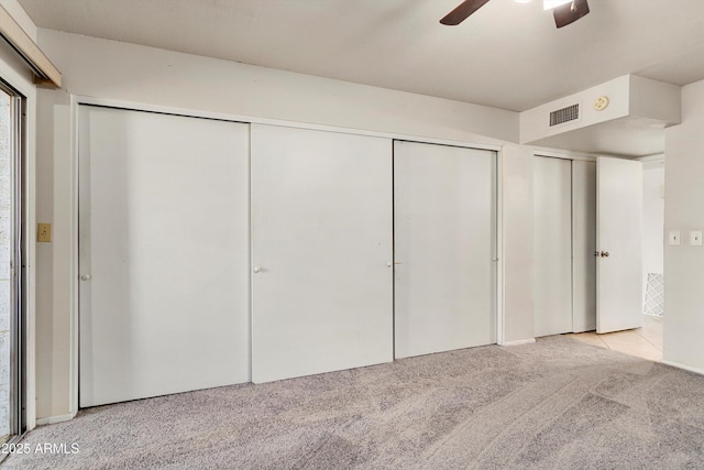 unfurnished bedroom featuring ceiling fan, visible vents, two closets, and light carpet