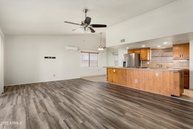 kitchen featuring brown cabinetry, light wood finished floors, ceiling fan, stainless steel fridge, and open floor plan