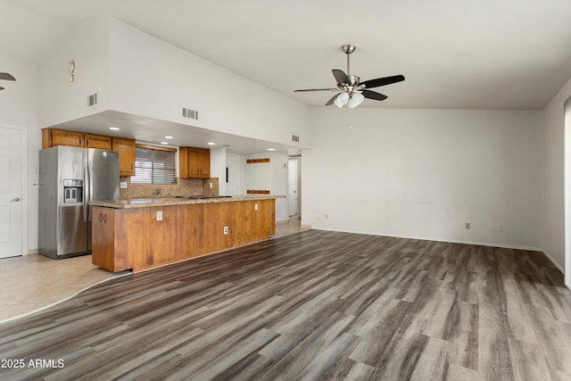 kitchen with visible vents, ceiling fan, open floor plan, stainless steel refrigerator with ice dispenser, and brown cabinetry