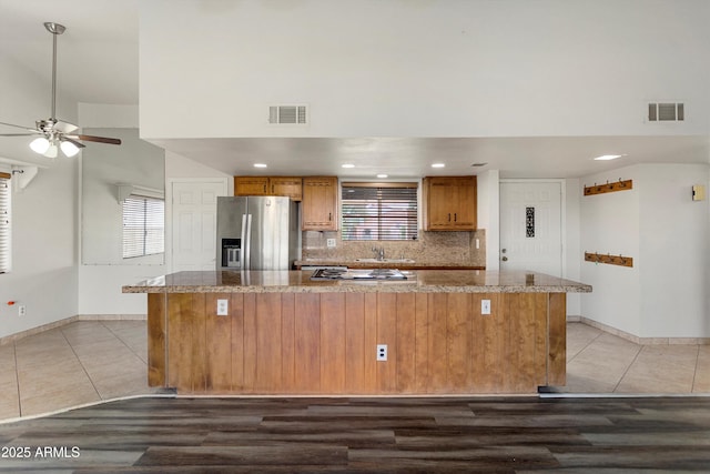 kitchen with decorative backsplash, visible vents, stainless steel refrigerator with ice dispenser, and brown cabinets