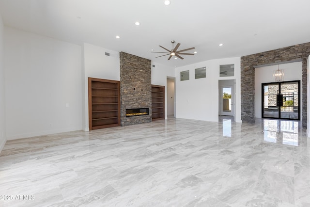 unfurnished living room featuring built in shelves, a stone fireplace, and ceiling fan with notable chandelier