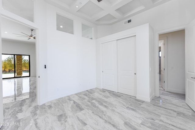 unfurnished bedroom featuring beamed ceiling, a high ceiling, coffered ceiling, and a closet