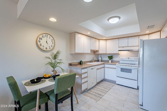 kitchen with a raised ceiling, sink, white cabinets, and white appliances