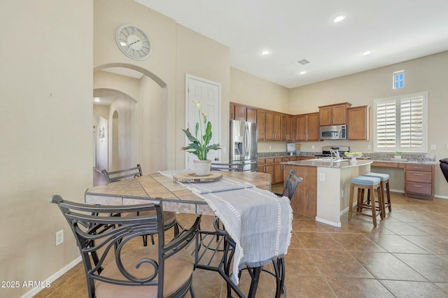 kitchen featuring appliances with stainless steel finishes, a kitchen breakfast bar, a high ceiling, a kitchen island with sink, and tile patterned floors