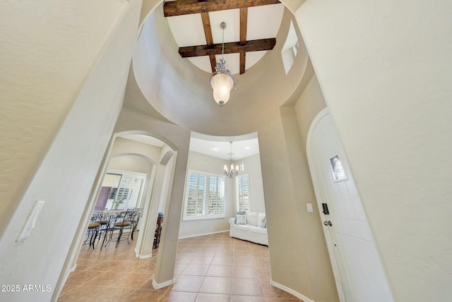 tiled foyer entrance with a notable chandelier, a towering ceiling, and beamed ceiling