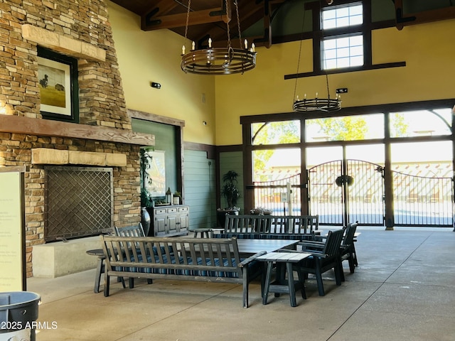 interior space with a stone fireplace, concrete floors, a high ceiling, a notable chandelier, and beam ceiling