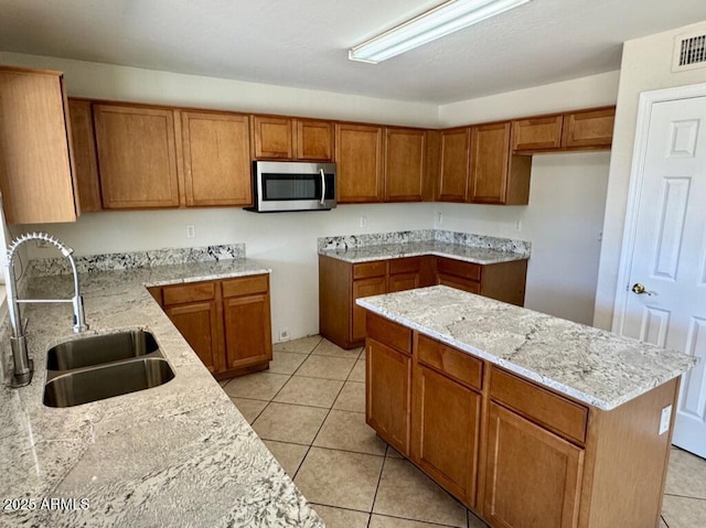 2634 S 63rd Dr, Phoenix, AZ 85043 - kitchen featuring stainless steel microwave, brown cabinetry, light stone countertops, and light tile patterned floors