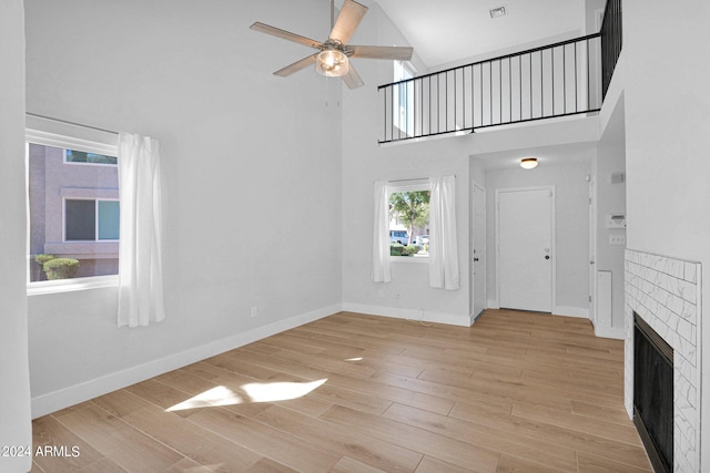 unfurnished living room with a brick fireplace, light hardwood / wood-style floors, a high ceiling, and ceiling fan