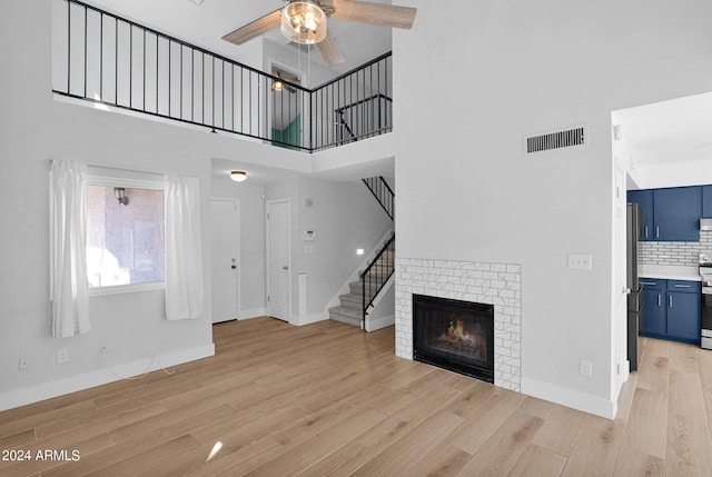 unfurnished living room with a fireplace, ceiling fan, a towering ceiling, and light hardwood / wood-style floors