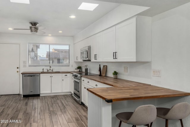 kitchen with white cabinets, appliances with stainless steel finishes, wood counters, ceiling fan, and a breakfast bar