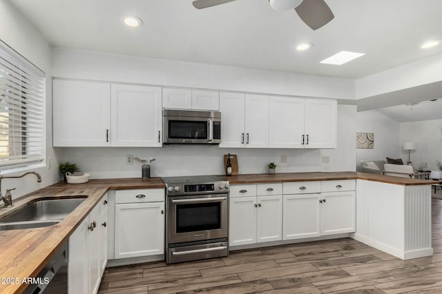 kitchen with white cabinetry, kitchen peninsula, wooden counters, appliances with stainless steel finishes, and sink