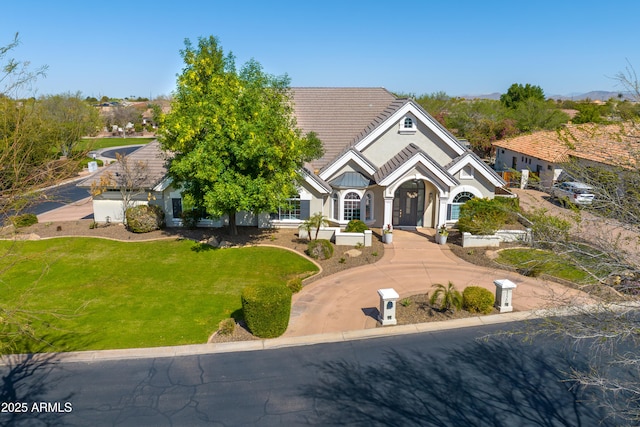 view of front of property featuring a front lawn, stucco siding, a tile roof, and curved driveway