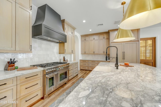 kitchen with visible vents, range with two ovens, light stone counters, custom exhaust hood, and a sink