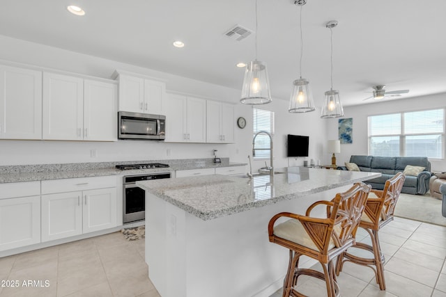 kitchen with appliances with stainless steel finishes, white cabinets, a kitchen island with sink, and open floor plan