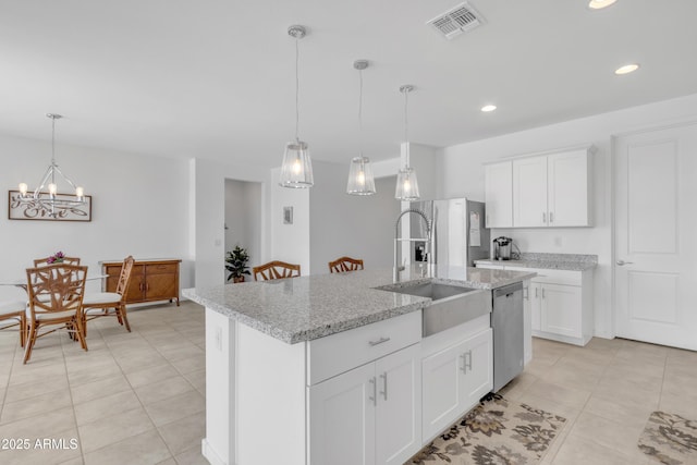 kitchen with pendant lighting, stainless steel appliances, a center island with sink, and white cabinetry