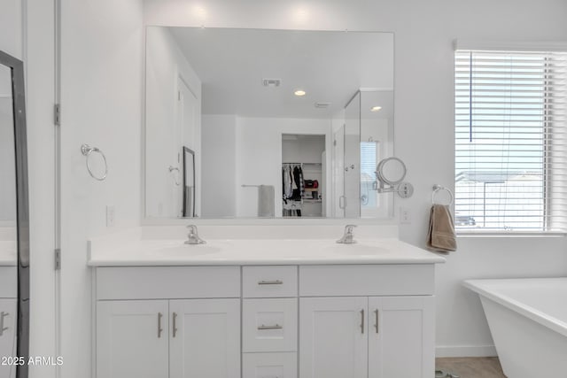 full bath featuring a freestanding bath, double vanity, a sink, and visible vents