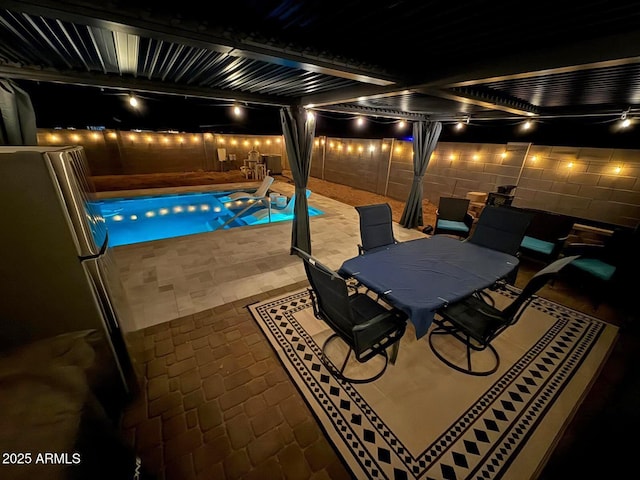 pool at night with a fenced backyard, outdoor dining area, a fenced in pool, and a patio