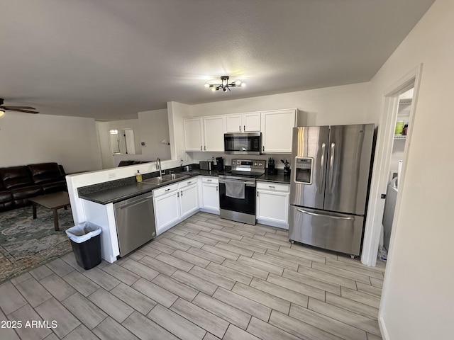 kitchen with white cabinets, dark countertops, open floor plan, stainless steel appliances, and a sink