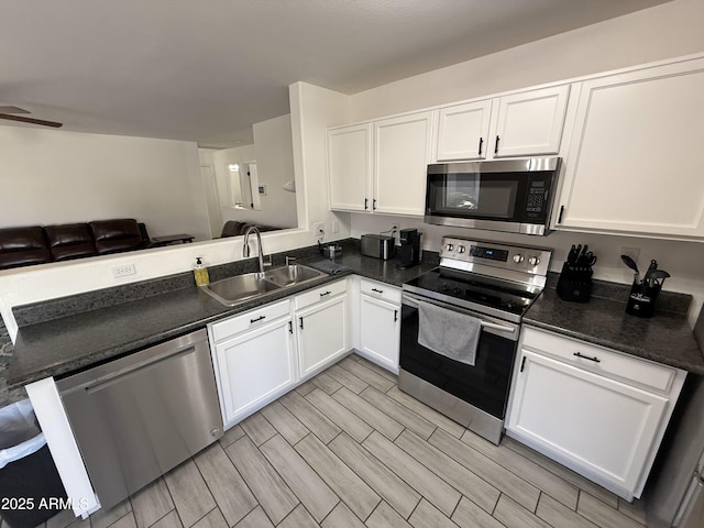 kitchen featuring appliances with stainless steel finishes, dark countertops, a sink, and white cabinets