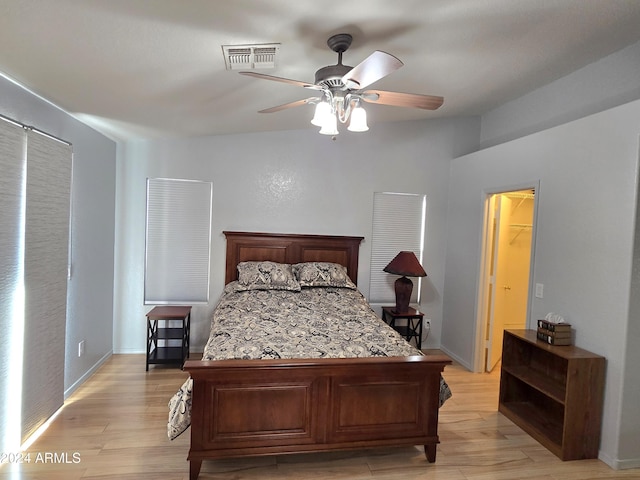 bedroom featuring a walk in closet, light hardwood / wood-style floors, a closet, and ceiling fan