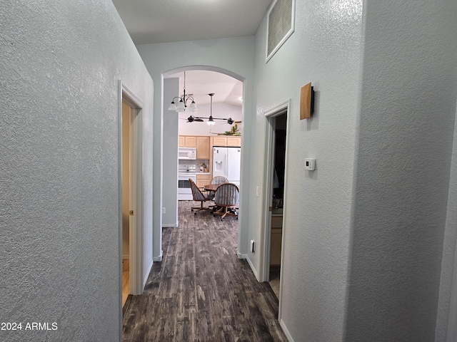 corridor with dark hardwood / wood-style flooring, vaulted ceiling, and a notable chandelier