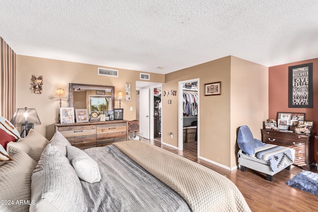 bedroom featuring a walk in closet, a closet, wood-type flooring, and a textured ceiling