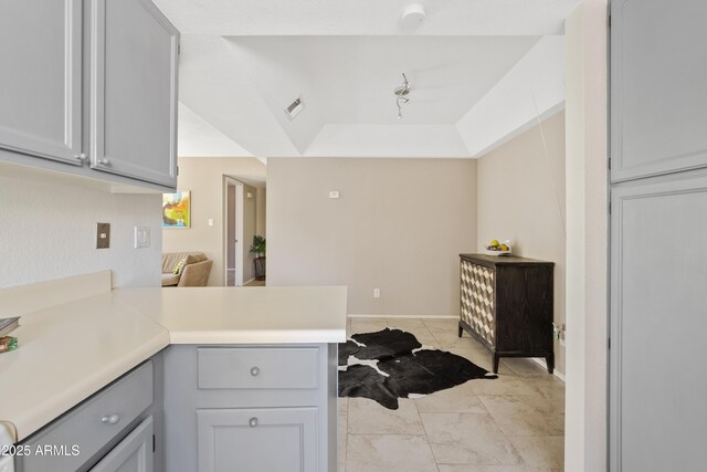 kitchen featuring light tile patterned flooring, kitchen peninsula, a raised ceiling, and gray cabinetry