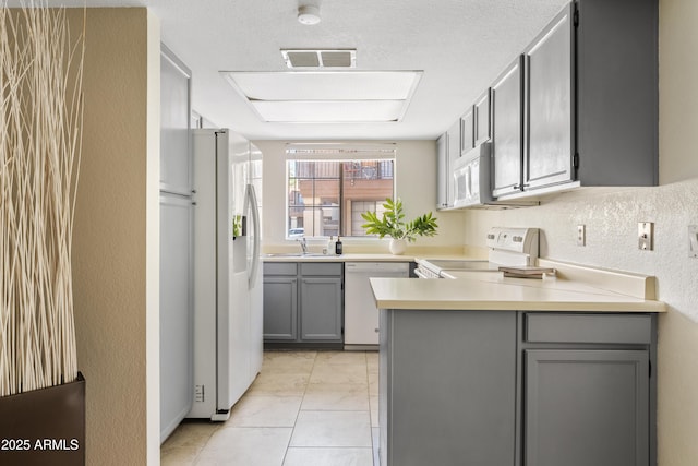 kitchen featuring sink, light tile patterned floors, gray cabinets, kitchen peninsula, and white appliances