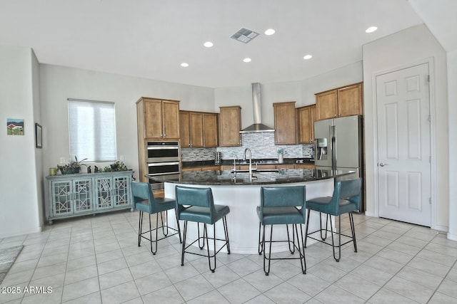 kitchen with decorative backsplash, a kitchen island with sink, a breakfast bar, and wall chimney exhaust hood