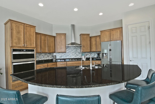 kitchen featuring sink, wall chimney exhaust hood, an island with sink, a kitchen bar, and appliances with stainless steel finishes