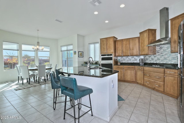 kitchen with a kitchen island with sink, an inviting chandelier, sink, wall chimney exhaust hood, and decorative light fixtures